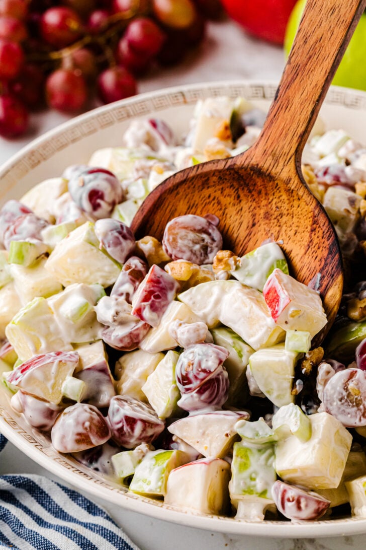 Bowl of Waldorf Salad in a white bowl being served with a wooden spoon.