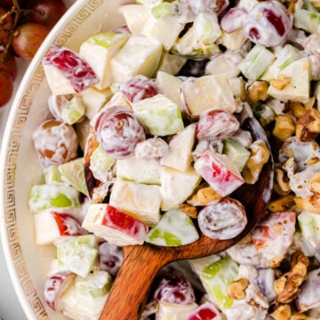 Waldorf salad 8 in white bowl with Greek key pattern, showing apples, celery, walnuts, and creamy dressing with wooden spoon