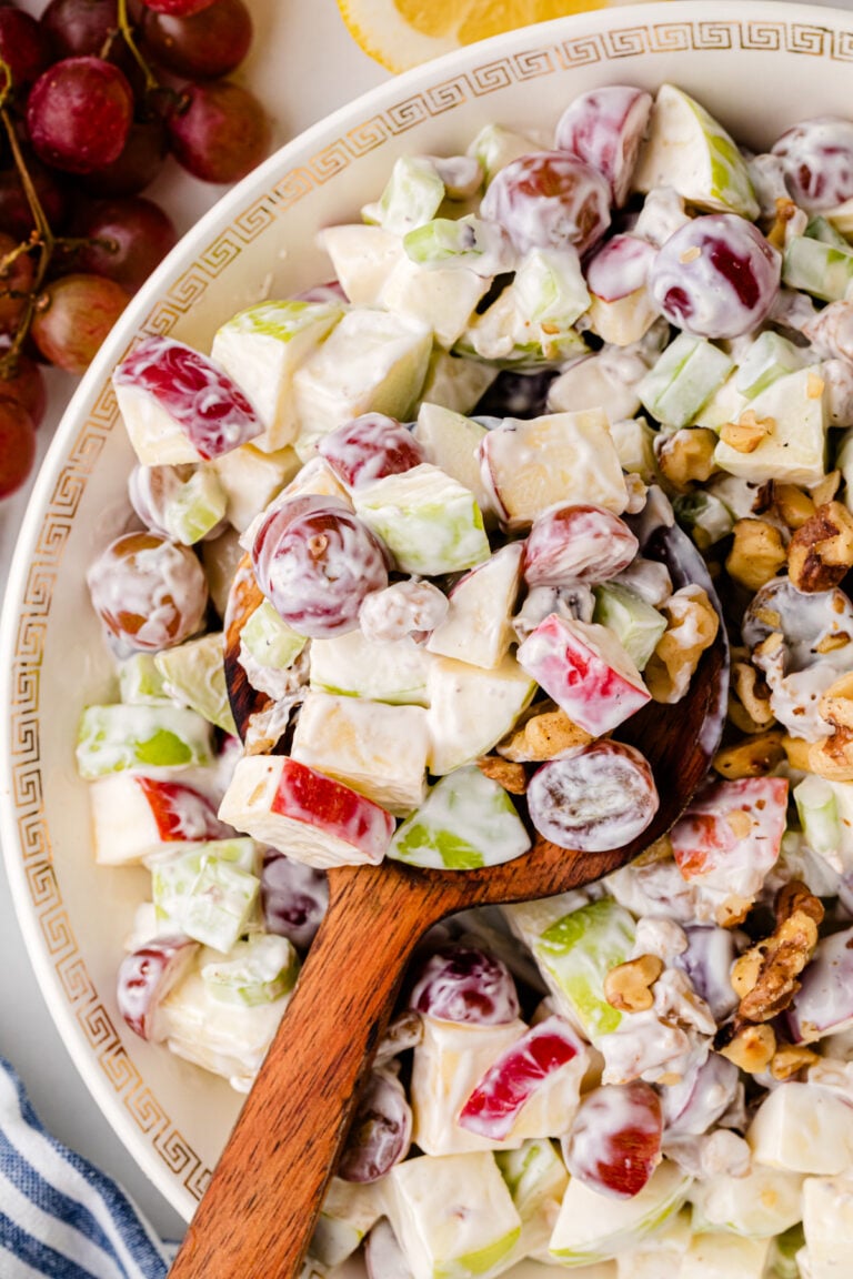 Waldorf salad 8 in white bowl with Greek key pattern, showing apples, celery, walnuts, and creamy dressing with wooden spoon