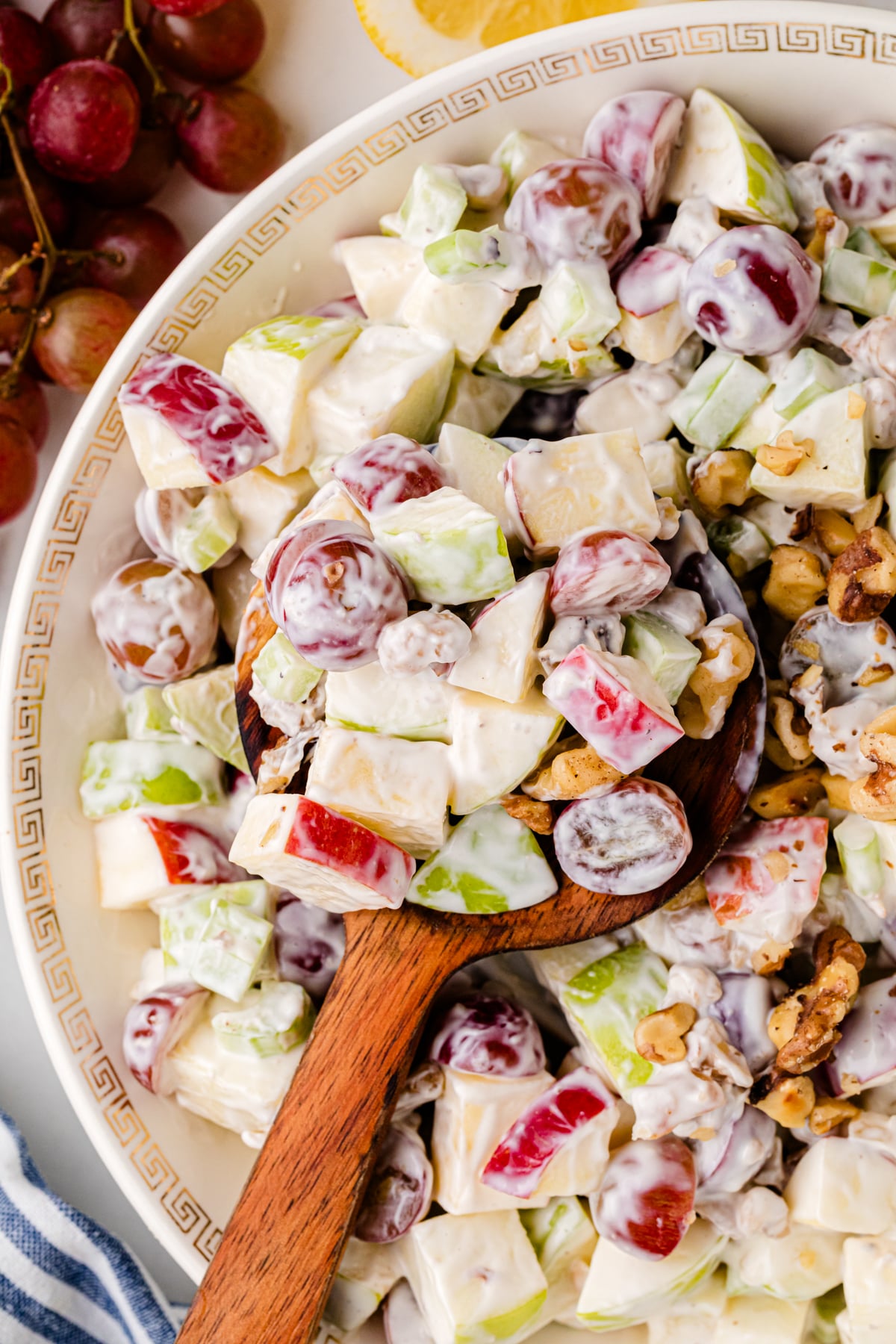 Waldorf salad 8 in white bowl with Greek key pattern, showing apples, celery, walnuts, and creamy dressing with wooden spoon