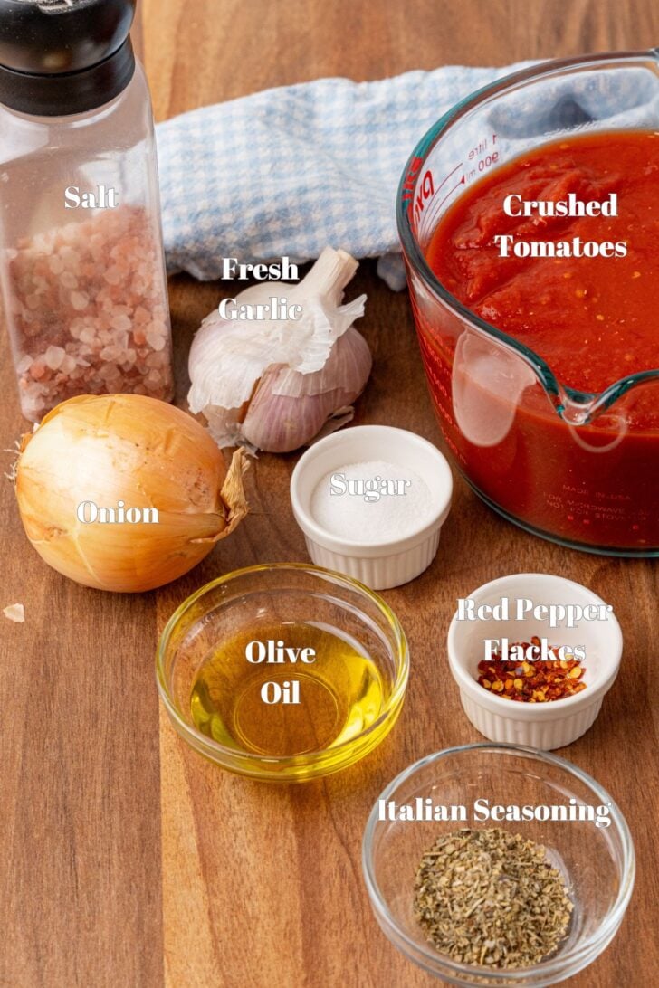 Ingredients for homemade marinara sauce in glass containers on a wooden cutting board.