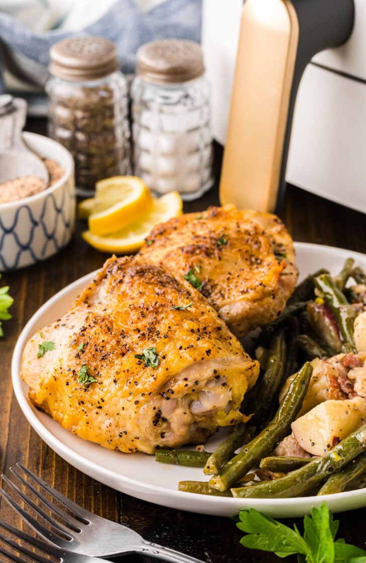 Air fried chicken thighs on a white plate served with green beans and potatoes.