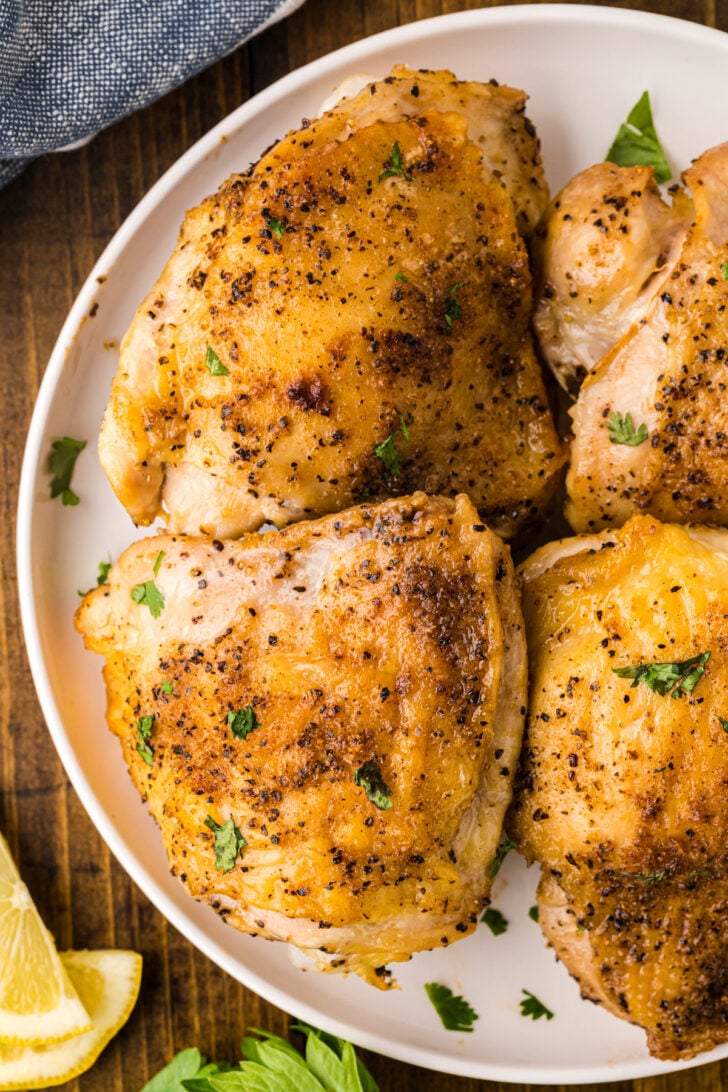 Golden brown chicken thighs cooked in an air fryer on a white plate.