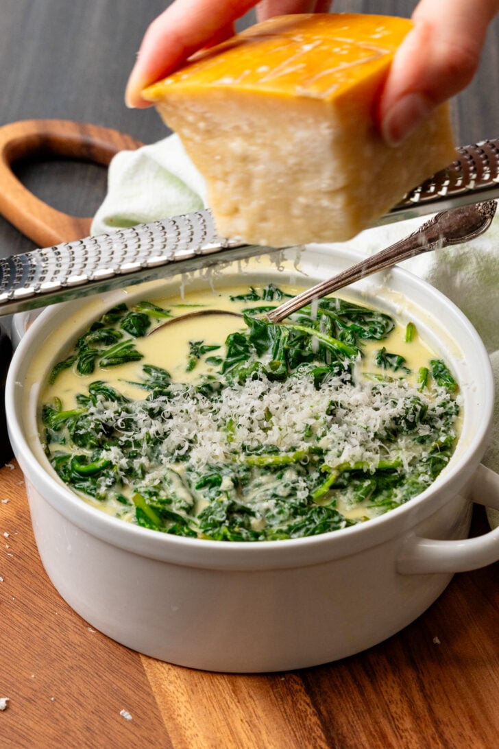 Parmesan cheese grated over a bowl of creamed spinach.