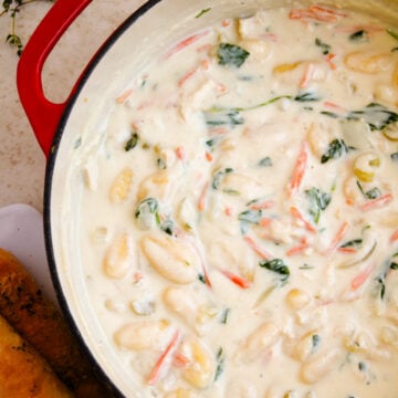 Creamy gnocchi soup 7 with shrimp and fresh herbs in a red-handled Dutch oven, overhead view on speckled countertop
