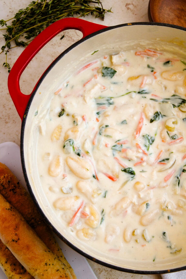 Creamy gnocchi soup 7 with shrimp and fresh herbs in a red-handled Dutch oven, overhead view on speckled countertop
