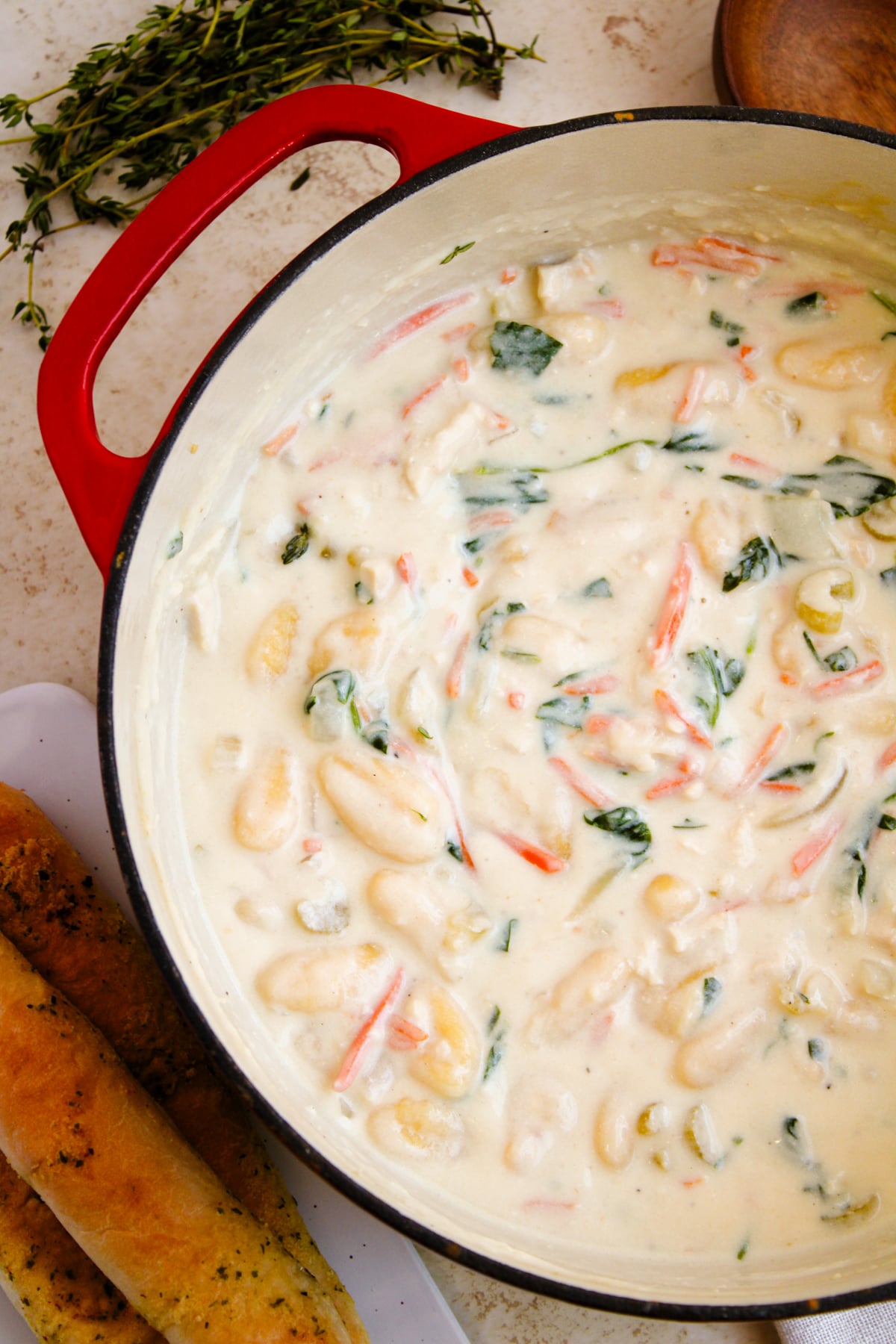Creamy gnocchi soup 7 with shrimp and fresh herbs in a red-handled Dutch oven, overhead view on speckled countertop