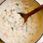 Creamy gnocchi soup 8 in red Dutch oven with wooden spoon, topped with fresh herbs and diced vegetables, overhead view