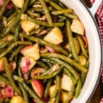 Southern Green Beans and Potatoes with bacon in a white bowl on a wooden table with red gingham cloth