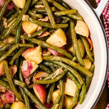 Southern Green Beans and Potatoes with bacon in a white bowl on a wooden table with red gingham cloth