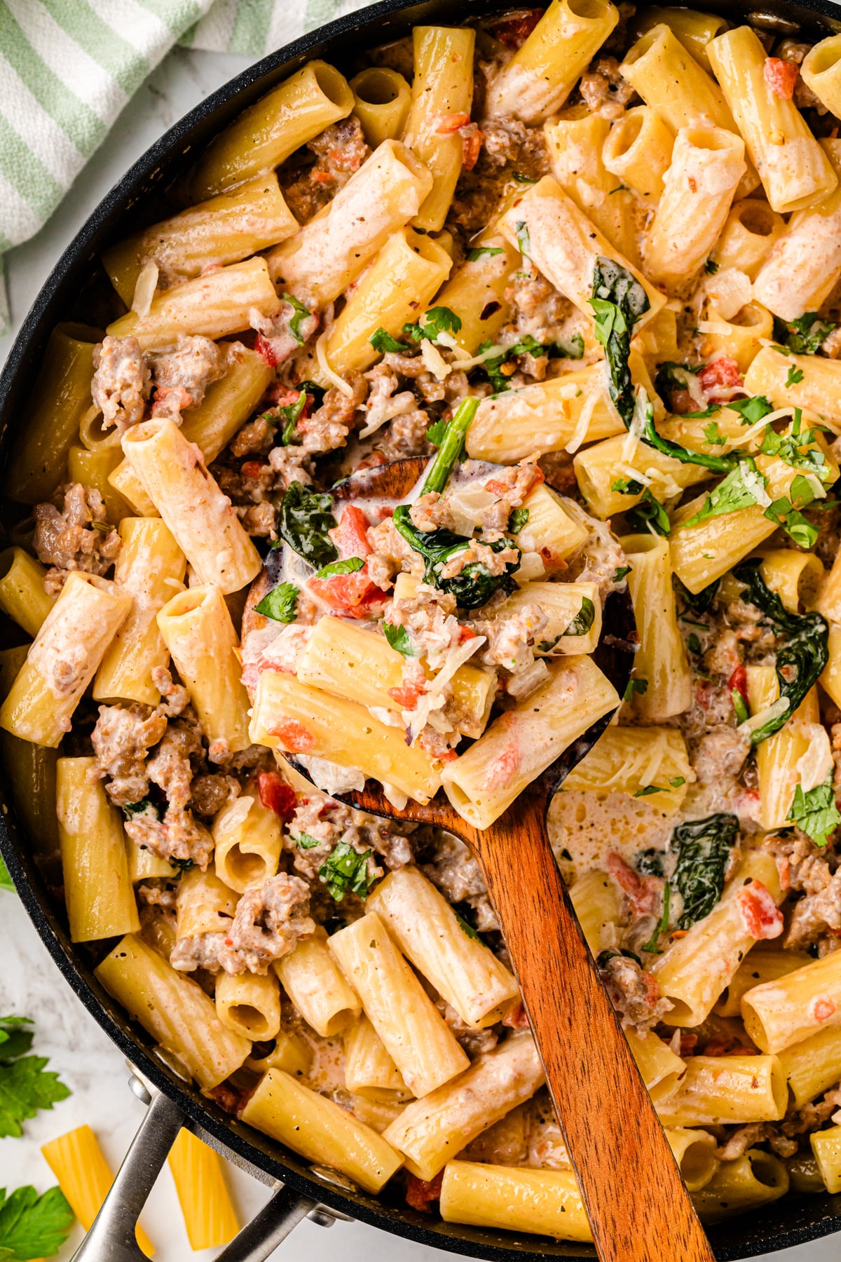 Italian sausage pasta with rigatoni, spinach, and diced tomatoes in a black skillet with wooden spoon