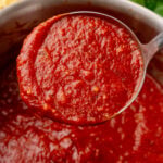 Homemade Marinara Sauce ladle dripping rich red tomato sauce into a pot, with fresh pasta and parsley visible nearby