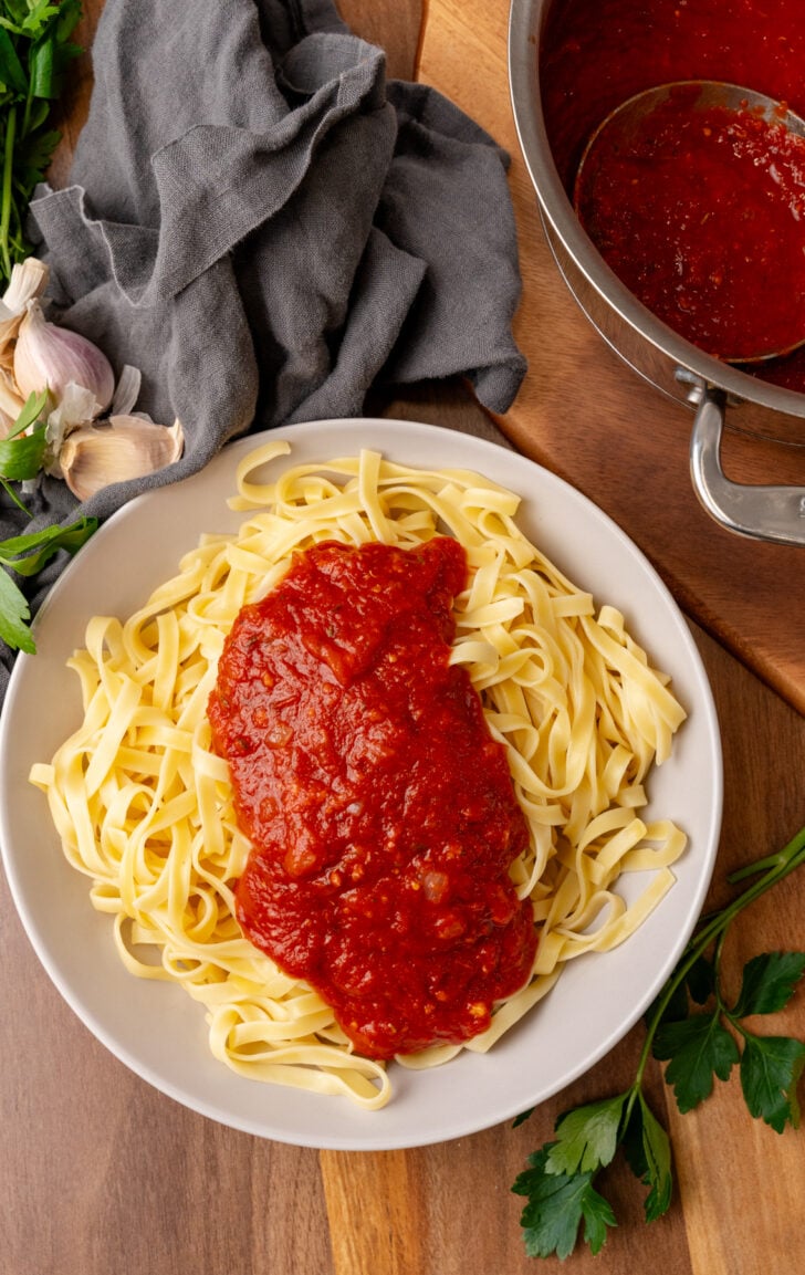 Homemade marinara sauce served over cooked pasta on a white plate.