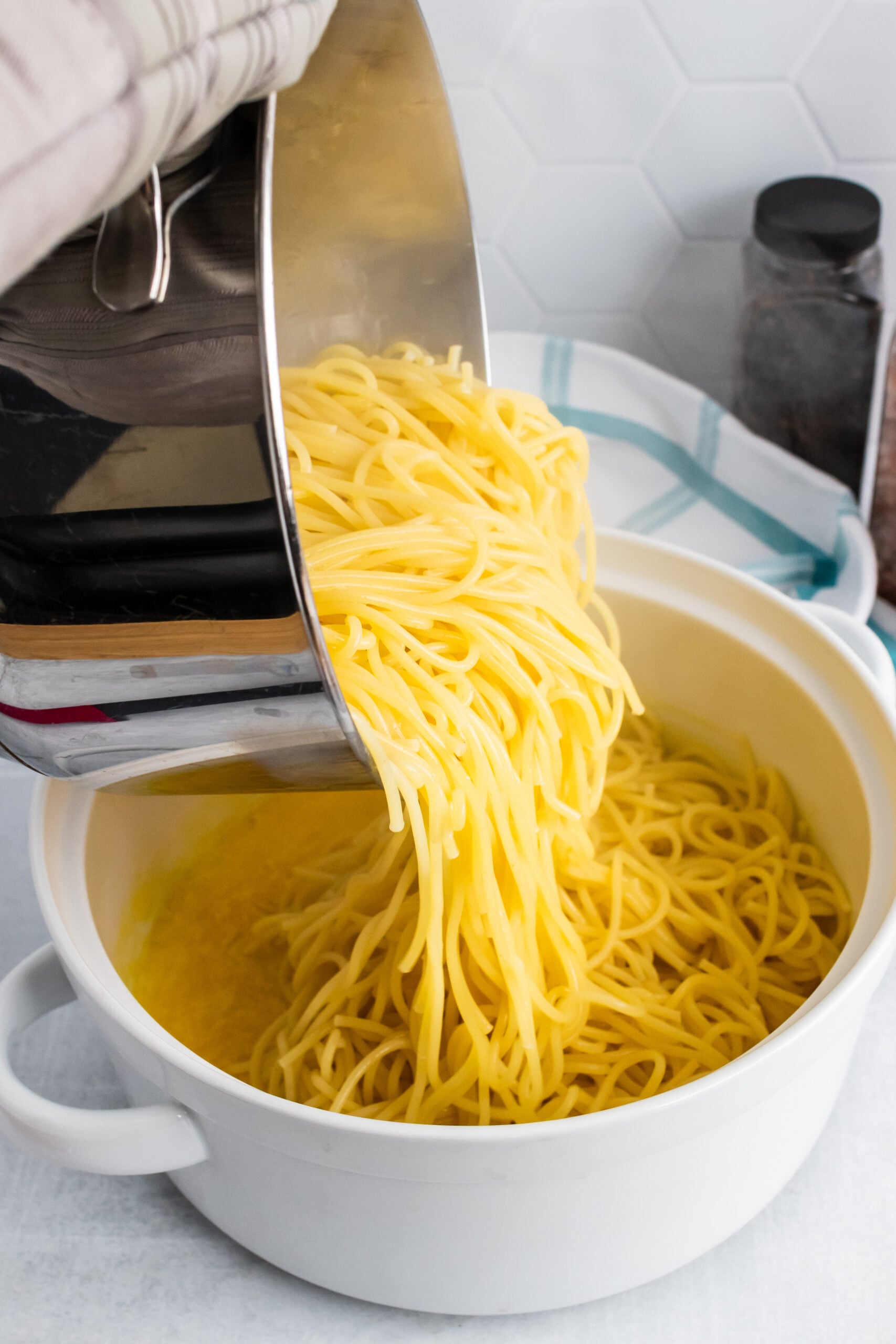 Draining cooked spaghetti noodles into white colander with golden broth, demonstrating Fall Pantry Essentials comfort cooking techniques