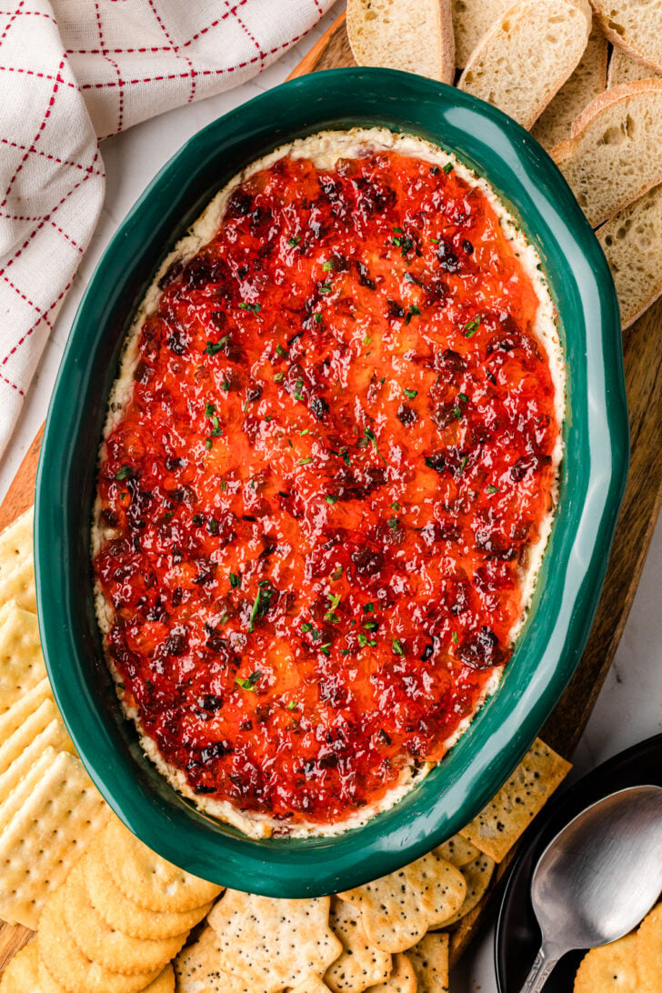 Pepper jelly cheese dip with bacon served in a green baking dish with crackers.