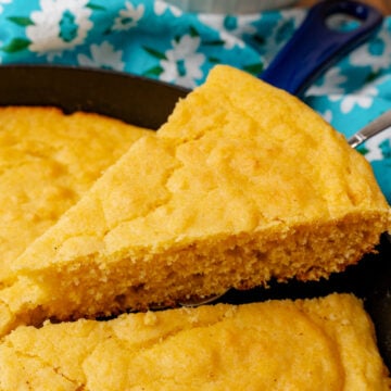 Slice of golden southern cornbread 6 on a knife with turquoise floral cloth and white bowl in background