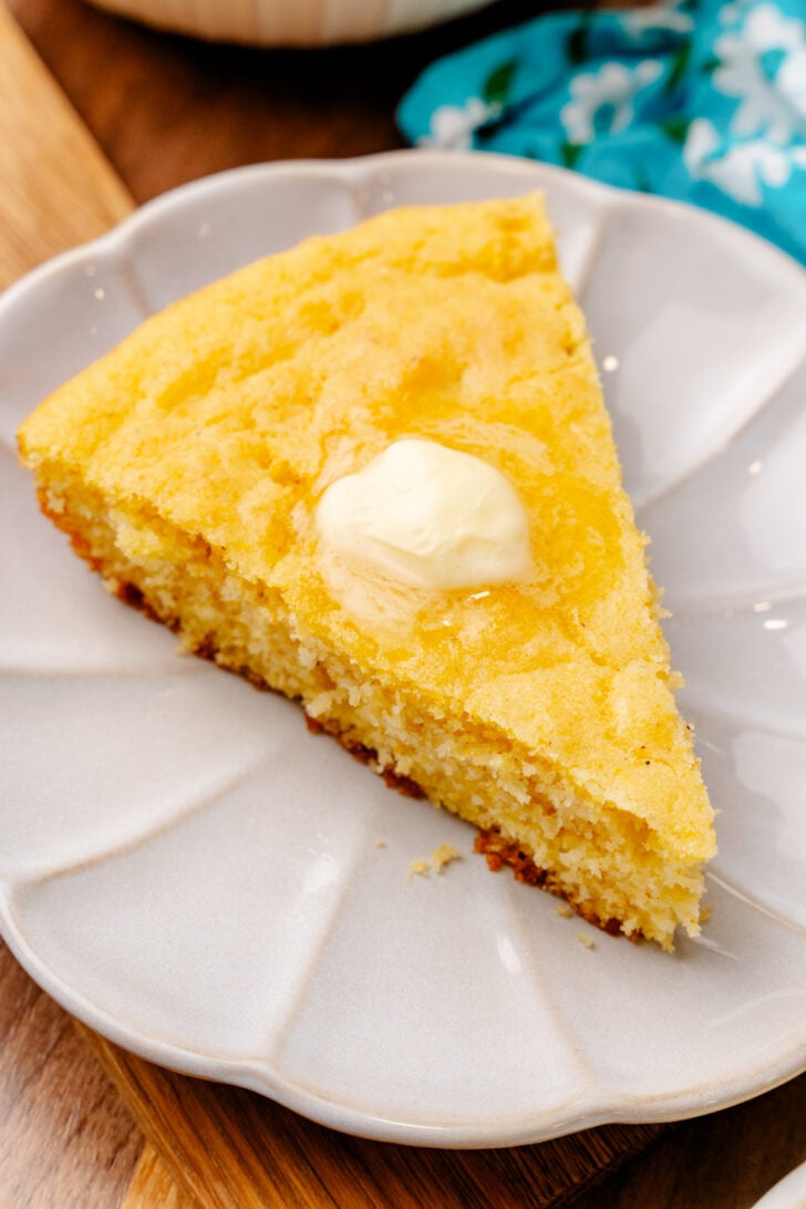 Slice of Southern cornbread with melted butter on a white plate.
