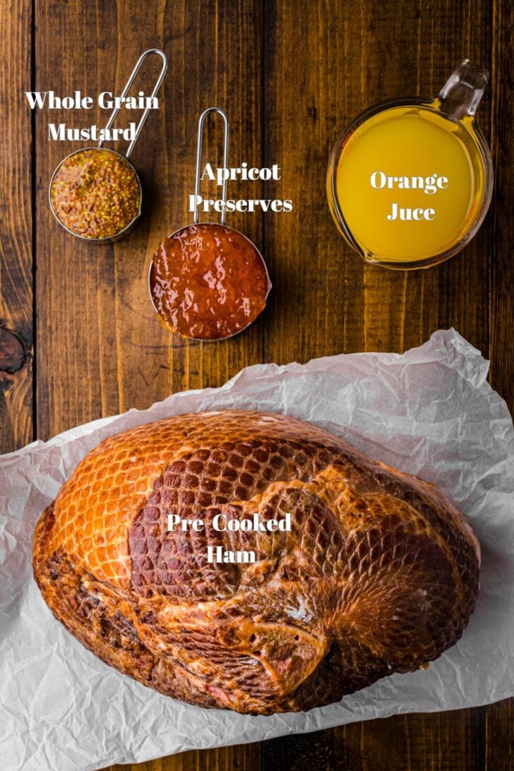 A wooden table with ingredients labeled: whole grain mustard, apricot preserves, orange juice, and a pre-cooked ham on parchment paper.