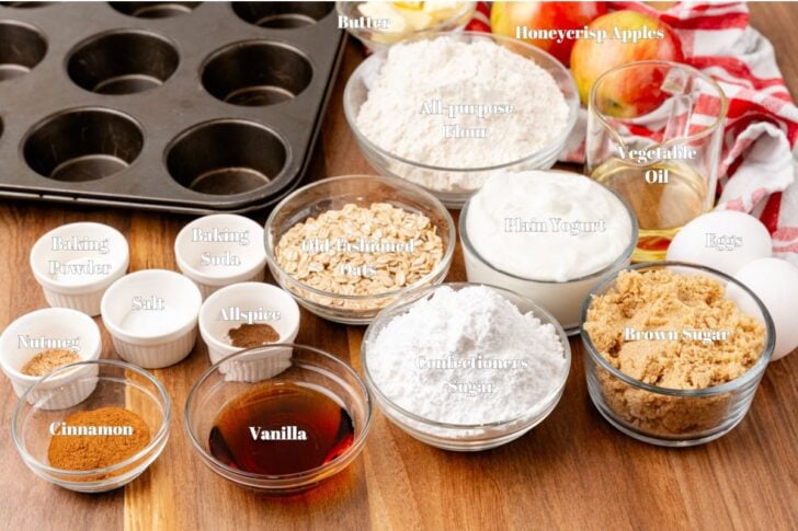 Overhead view of the ingredients for Honeycrisp Muffins neatly arranged in small bowls, including diced apples, flour, cinnamon, eggs, maple syrup, and butter.