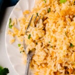 Mom's Baked Cheesy Rice served on a white plate with a fork, garnished with fresh parsley and green onions
