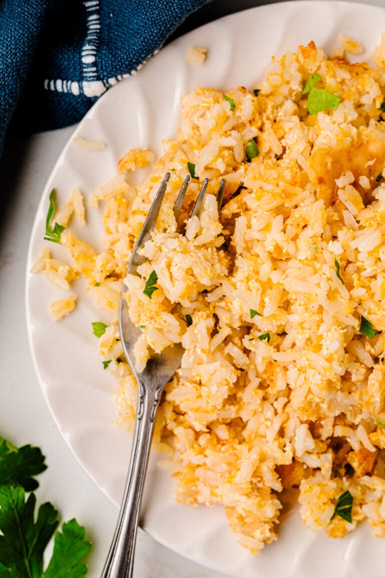 Mom's Baked Cheesy Rice served on a white plate with a fork, garnished with fresh parsley and green onions