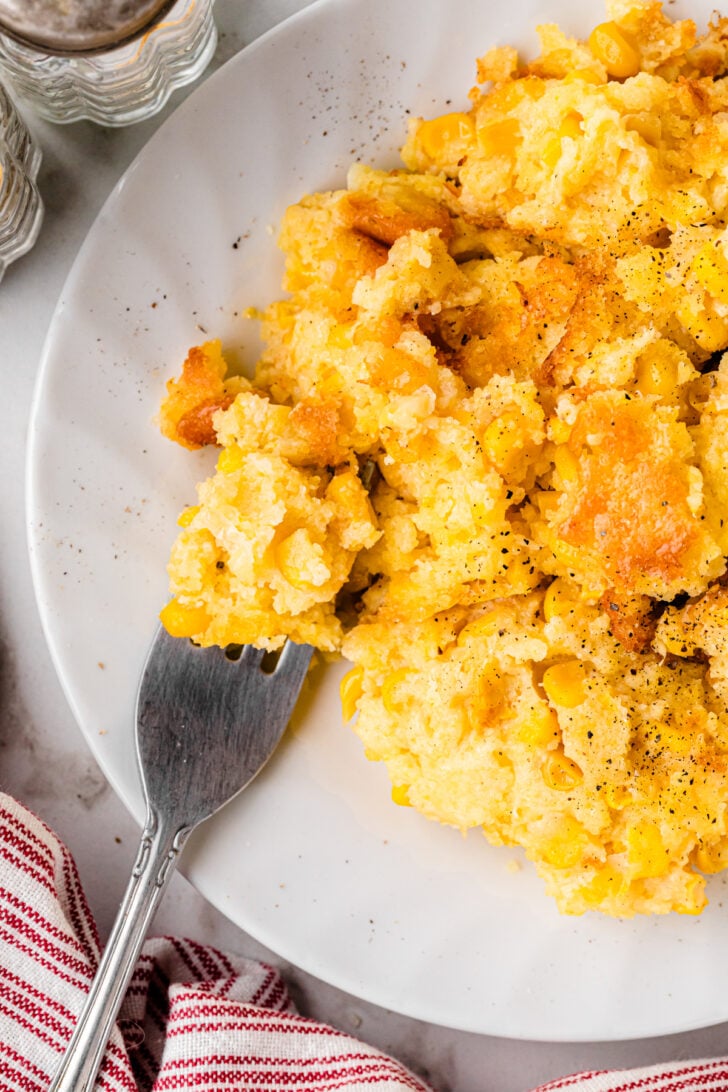 Baked cornbread pudding sprinkled with a pinch of black pepper served on a white plate.