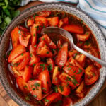 Marinated tomatoes 4 served in decorative bowl with fresh parsley garnish, spoon, and whole tomatoes visible in background on wooden surface