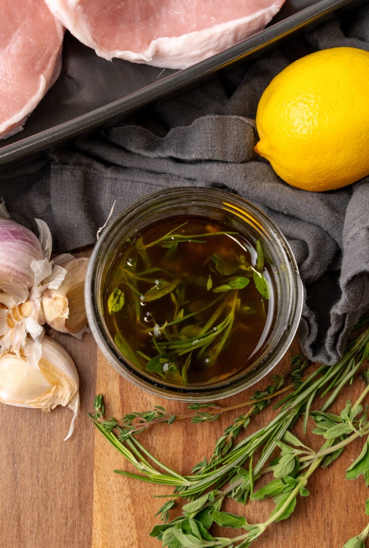 Glass jar filled with meat marinade and fresh herbs.