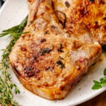 Seared pork chops with herb meat marinade 5, rosemary and thyme garnish on white plate, overhead view