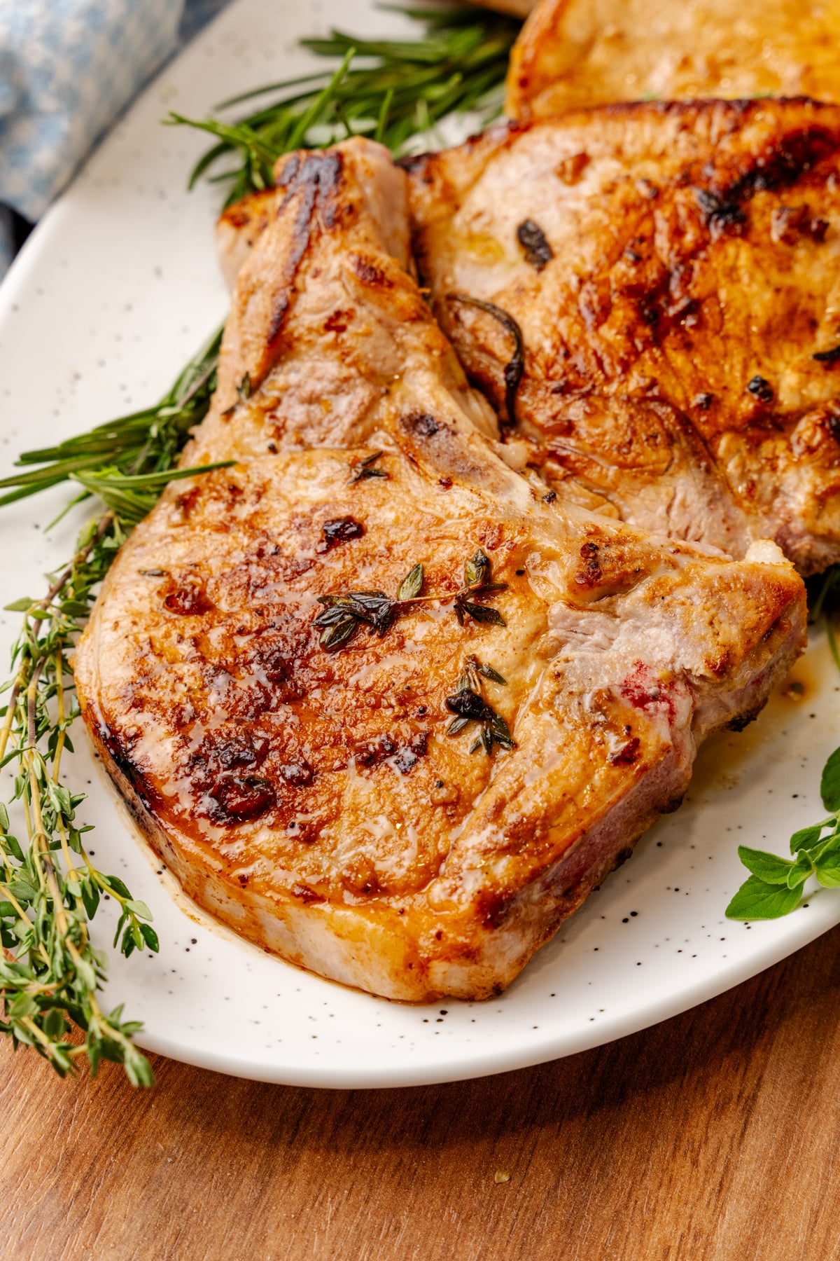 Seared pork chops with herb meat marinade 5, rosemary and thyme garnish on white plate, overhead view