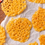 Golden parmesan crisps 5 cooling on parchment paper with wooden board and red checkered cloth visible