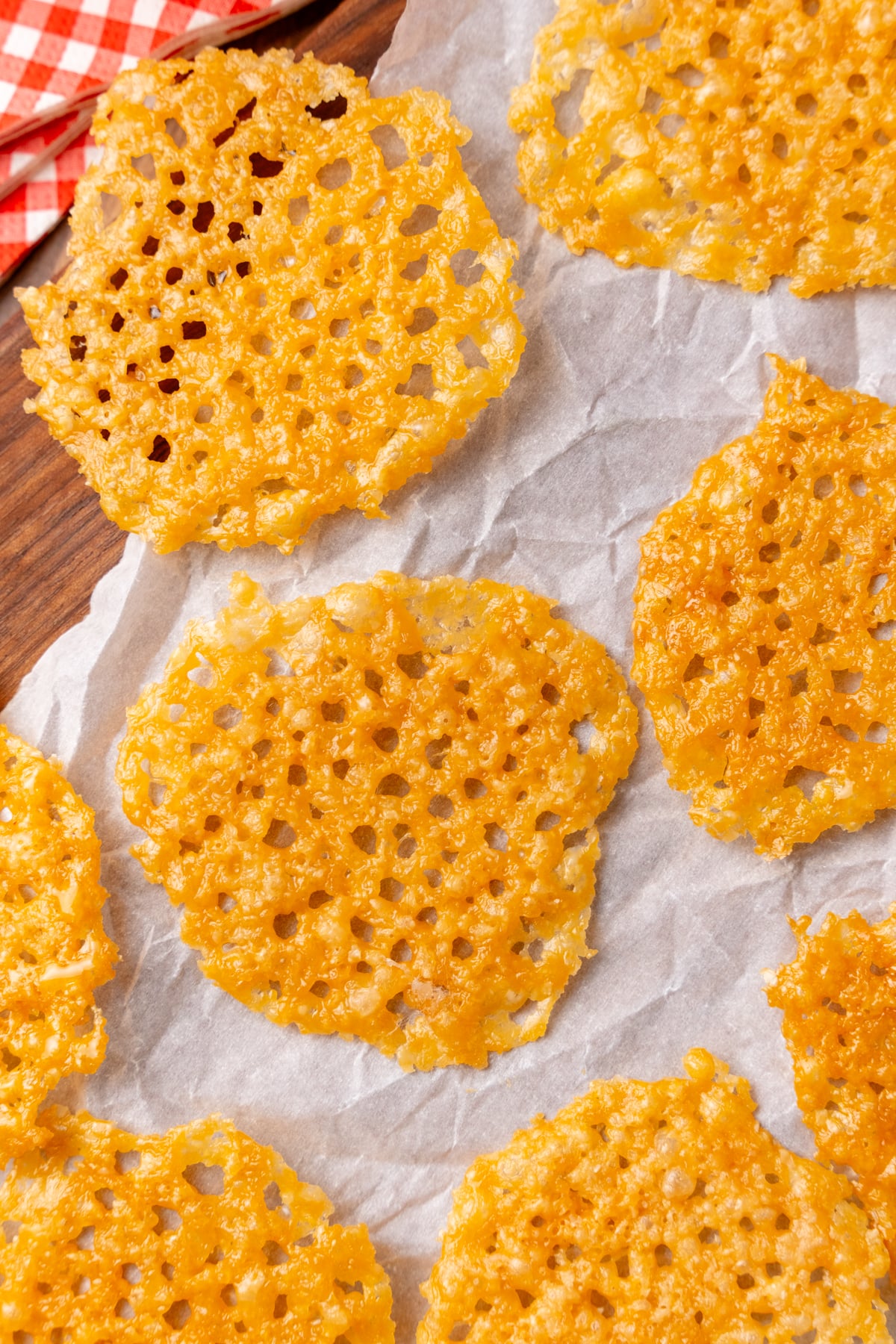 Golden parmesan crisps 5 cooling on parchment paper with wooden board and red checkered cloth visible