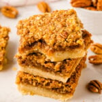 Stack of Southern Style Pecan Pie Bars with golden crumbly pecan topping and buttery shortbread base on white surface