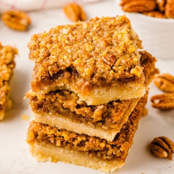 Stack of Southern Style Pecan Pie Bars with golden crumbly pecan topping and buttery shortbread base on white surface