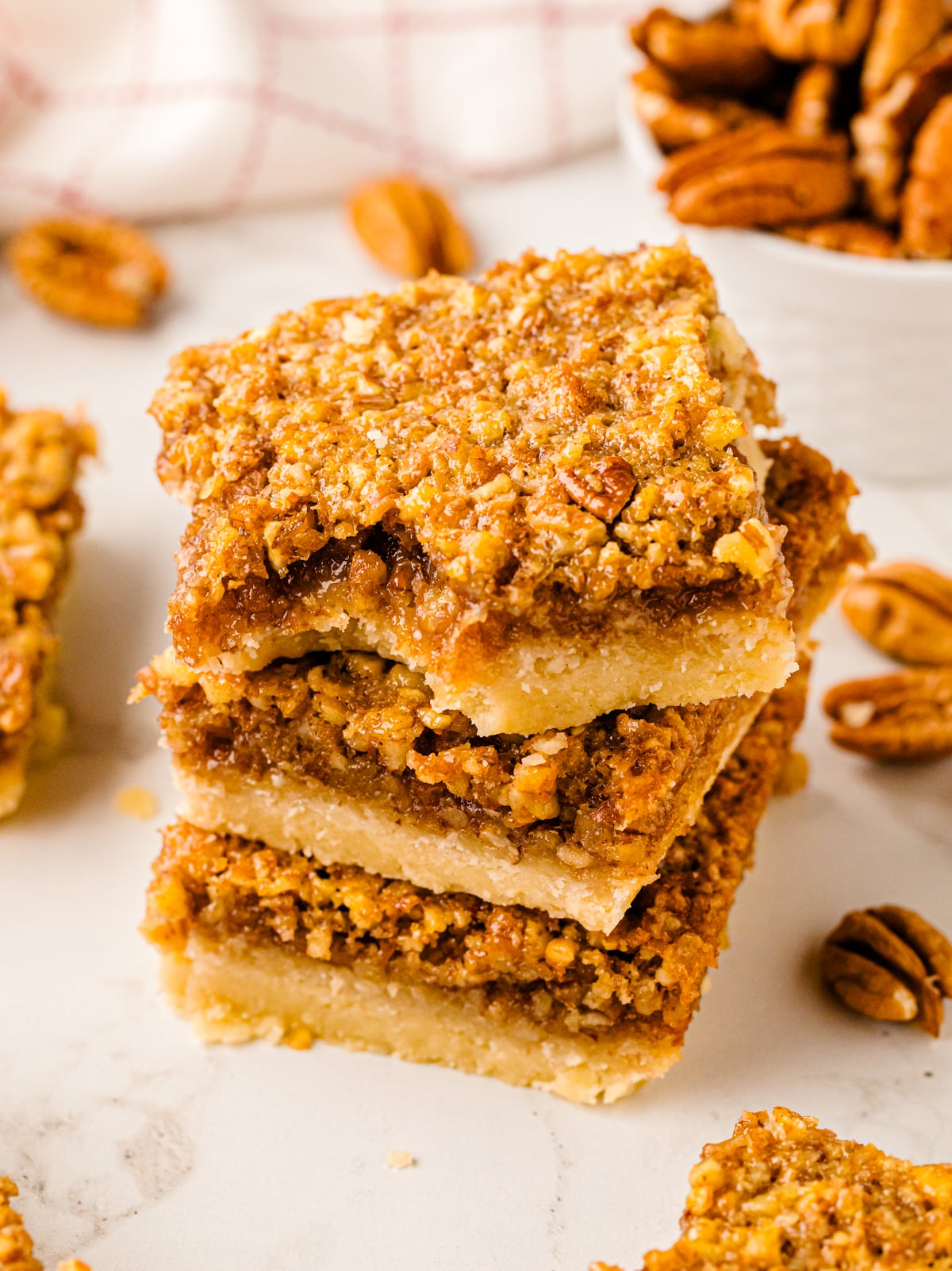 Stack of Southern Style Pecan Pie Bars with golden crumbly pecan topping and buttery shortbread base on white surface