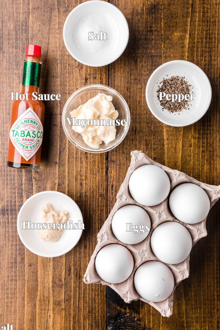 Boiled eggs, hot sauce, mayo, and seasoning on a wooden counter for Deviled Egg Recipe.