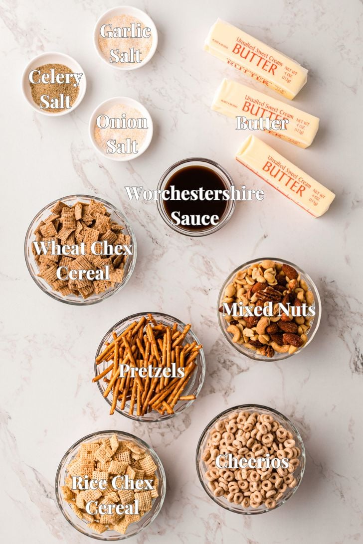 Ingredients for a snack mix on a marble surface: butter sticks, Worcestershire sauce, garlic salt, onion salt, celery salt, Wheat Chex cereal, Rice Chex cereal, pretzels, mixed nuts, and Cheerios in bowls.