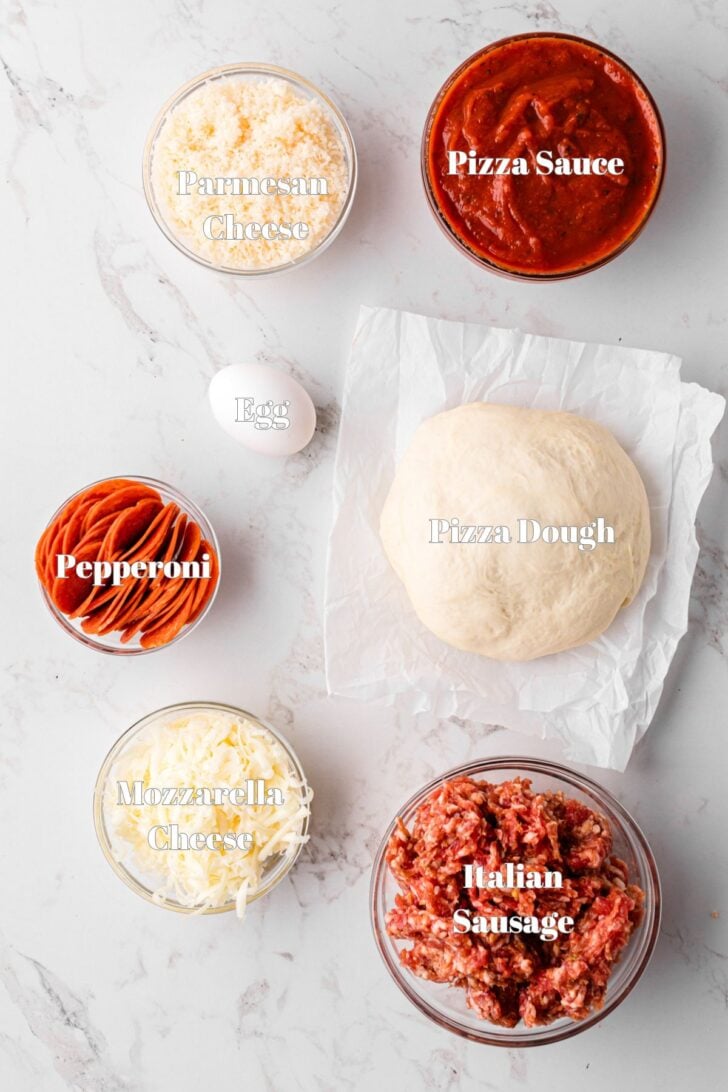 Seven easy ingredients on a white counter for homemade baked stromboli make with storebought pizza dough and sauce.