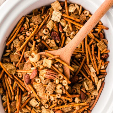 cp party mix 6 in white bowl with wooden spoon showing chex cereal, pretzels, nuts, and almonds mixed together
