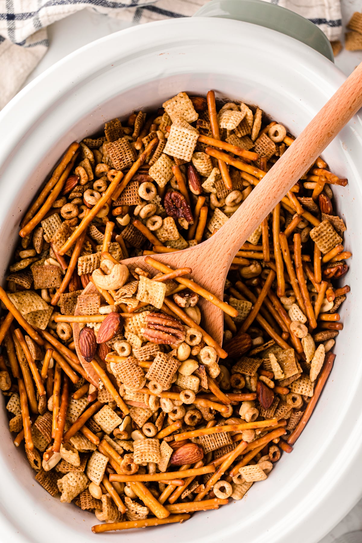 cp party mix 6 in white bowl with wooden spoon showing chex cereal, pretzels, nuts, and almonds mixed together