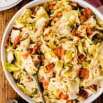 Fried cabbage with crispy bacon pieces served in a white bowl with a spoon, topped with red pepper flakes on wooden surface