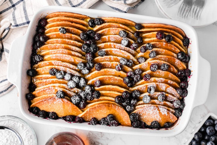 Make-Ahead Pancake Casserole: Easy, Fluffy, and Delicious baked in white dish with sliced apples, blueberries, and powdered sugar