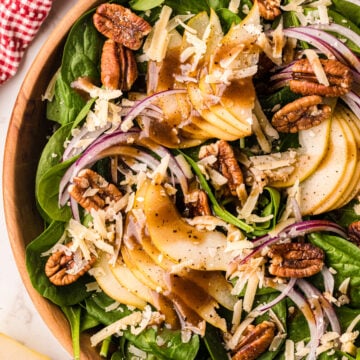 Spinach pear salad 3 in wooden bowl with candied pecans, shredded cheese, red onion, and black pepper, overhead view