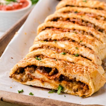 Sliced stromboli 6 with meat filling arranged on parchment paper on wooden board, garnished with fresh parsley and served with dipping sauce