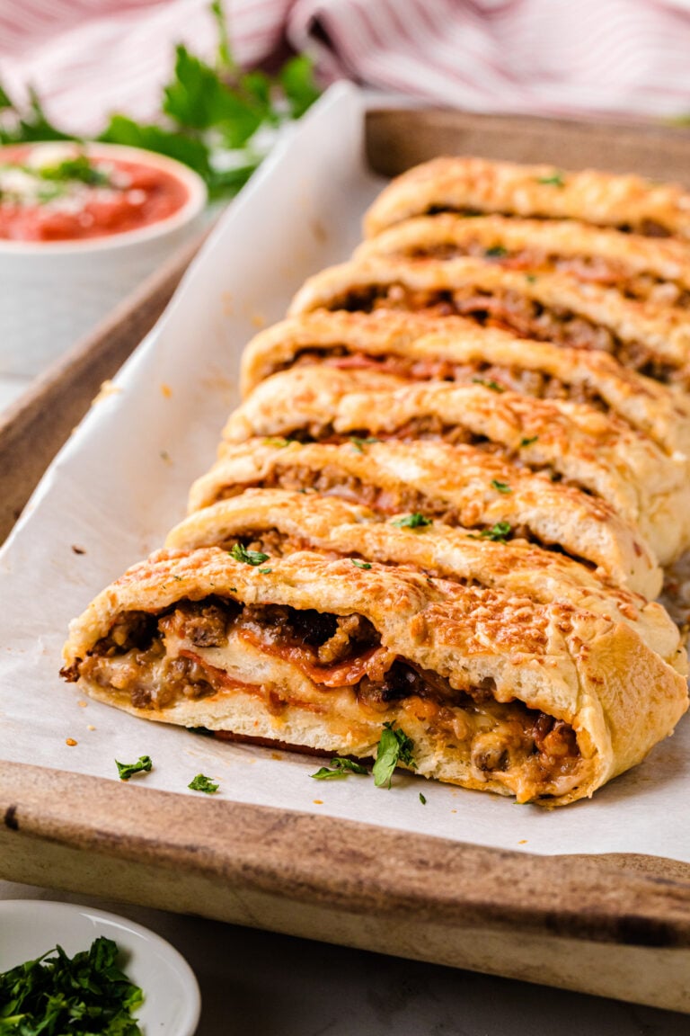 Sliced stromboli 6 with meat filling arranged on parchment paper on wooden board, garnished with fresh parsley and served with dipping sauce