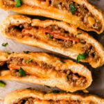 Beef stromboli 8 1 sliced and stacked on parchment paper, topped with melted cheese, caramelized onions, and fresh parsley garnish