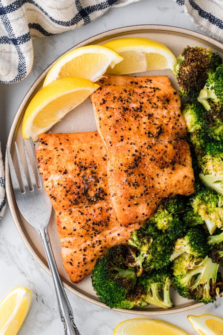 A plate with seasoned salmon fillets, steamed broccoli, and lemon wedges. A fork rests beside the plate.