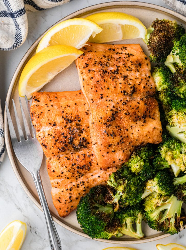 Plated airfryer salmon 10 e1755524148211 with crispy blackened seasoning, roasted broccoli, and lemon wedges on ceramic dish with fork