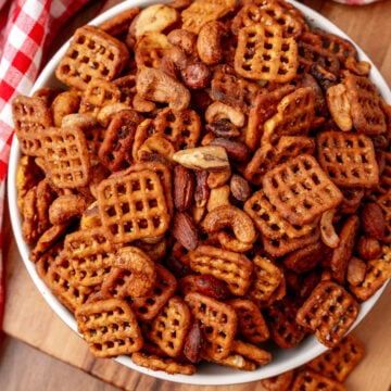 Buffalo snack mix 7 with waffle crackers and roasted nuts in white bowl on wooden board with red checkered cloth
