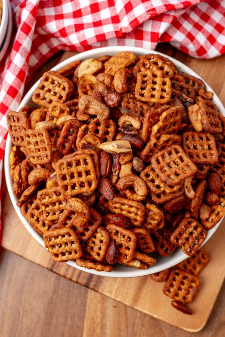 Buffalo snack mix 7 with waffle crackers and roasted nuts in white bowl on wooden board with red checkered cloth